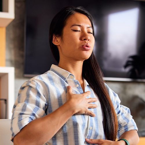 Mulher com a mão no peito e expressão de desconforto, sugerindo sensação de queimação ou dificuldade para respirar.